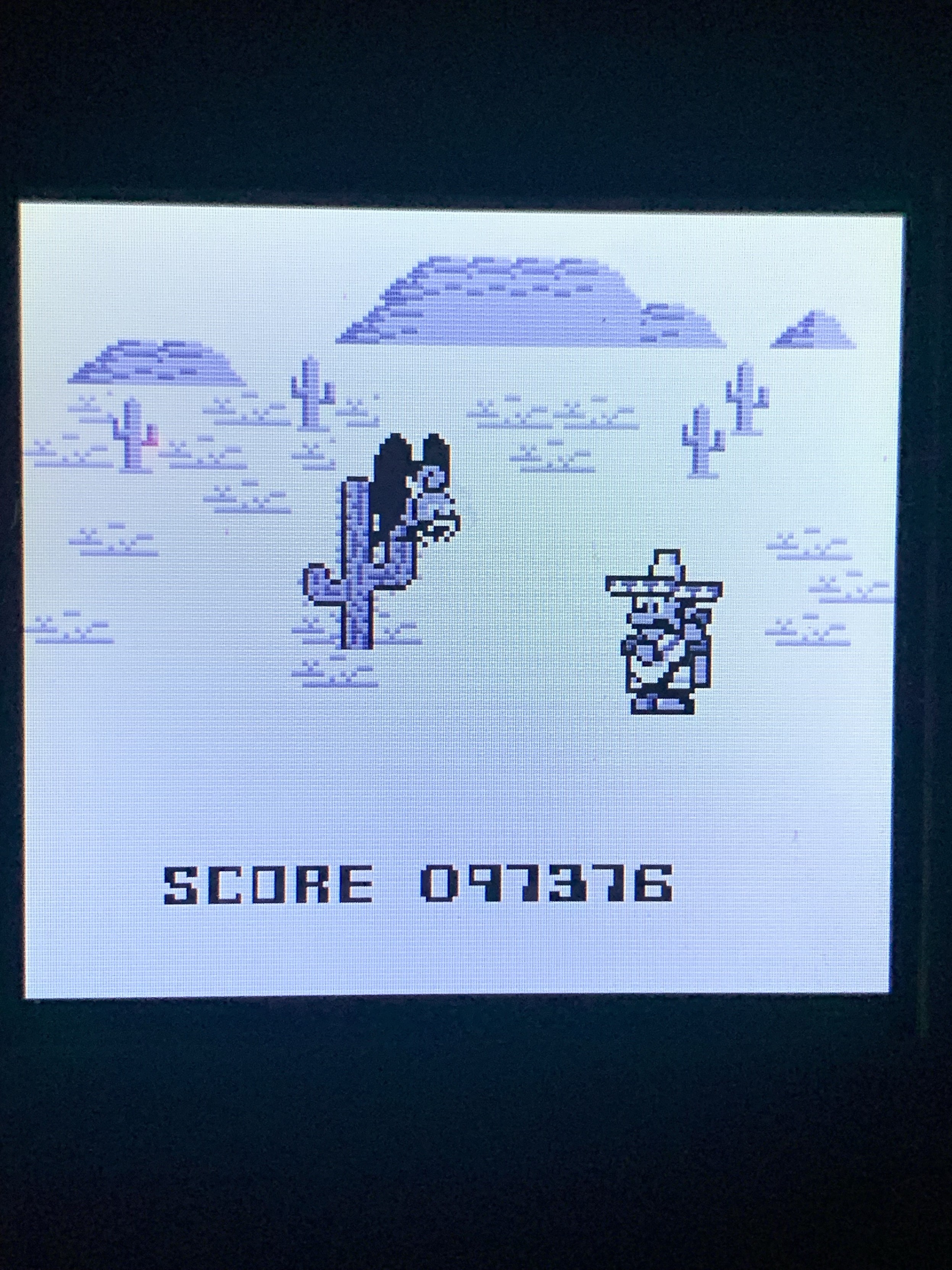 A retro video game screen displaying a cowboy facing a horse with cacti and hills in the background. The score is displayed at the bottom, showing 097376. The image uses a monochrome pixel art style.