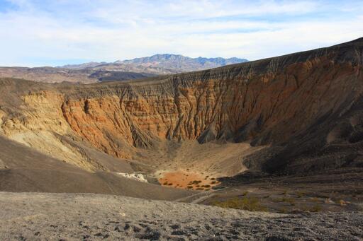 The half-mile deep Ubehebe crater in DVNP, showing distinct sedimentary layers on the crater walls, the lower of which are a striking orange color.