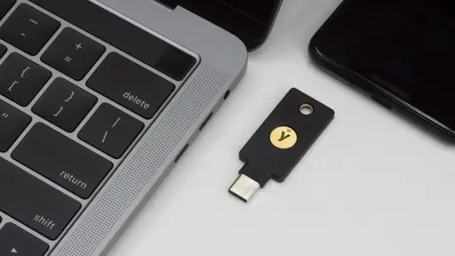 Photo of a YubiKey security key on a table between a MacBook computer and a cellphone.