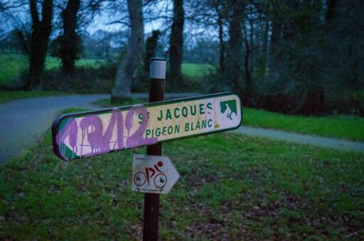 "1312" graffiti'd onto a direction sign pointing left to St Jacques Pigeon Blanc

park full of trees can be seen in the background