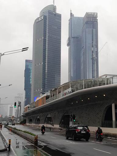 A bus stop that resembles a ship in a city full of skyscraper with a statue (Selamat Datang Monument) visible in the distance