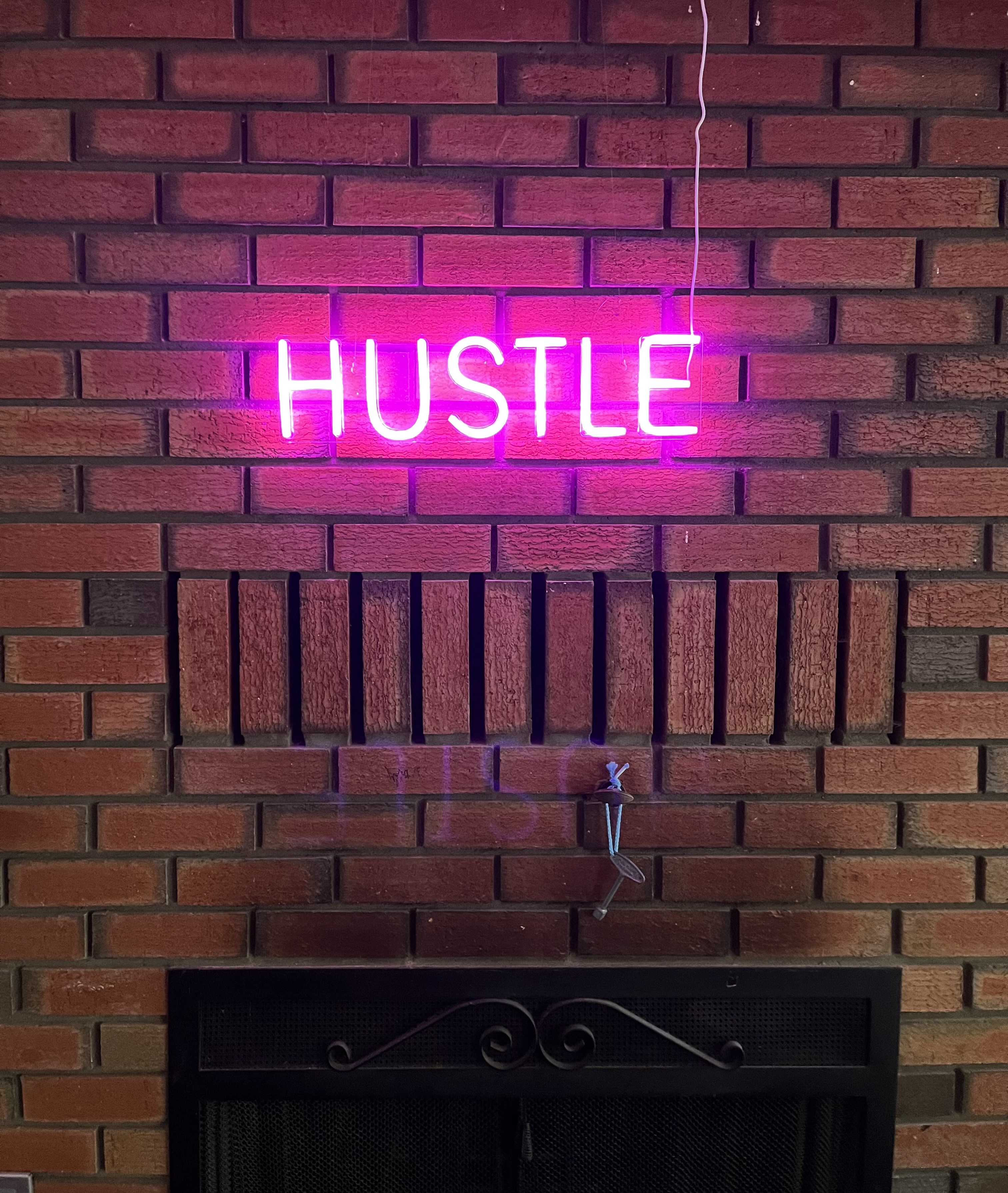 a brick wall with a neon pink light up sign saying “hustle”