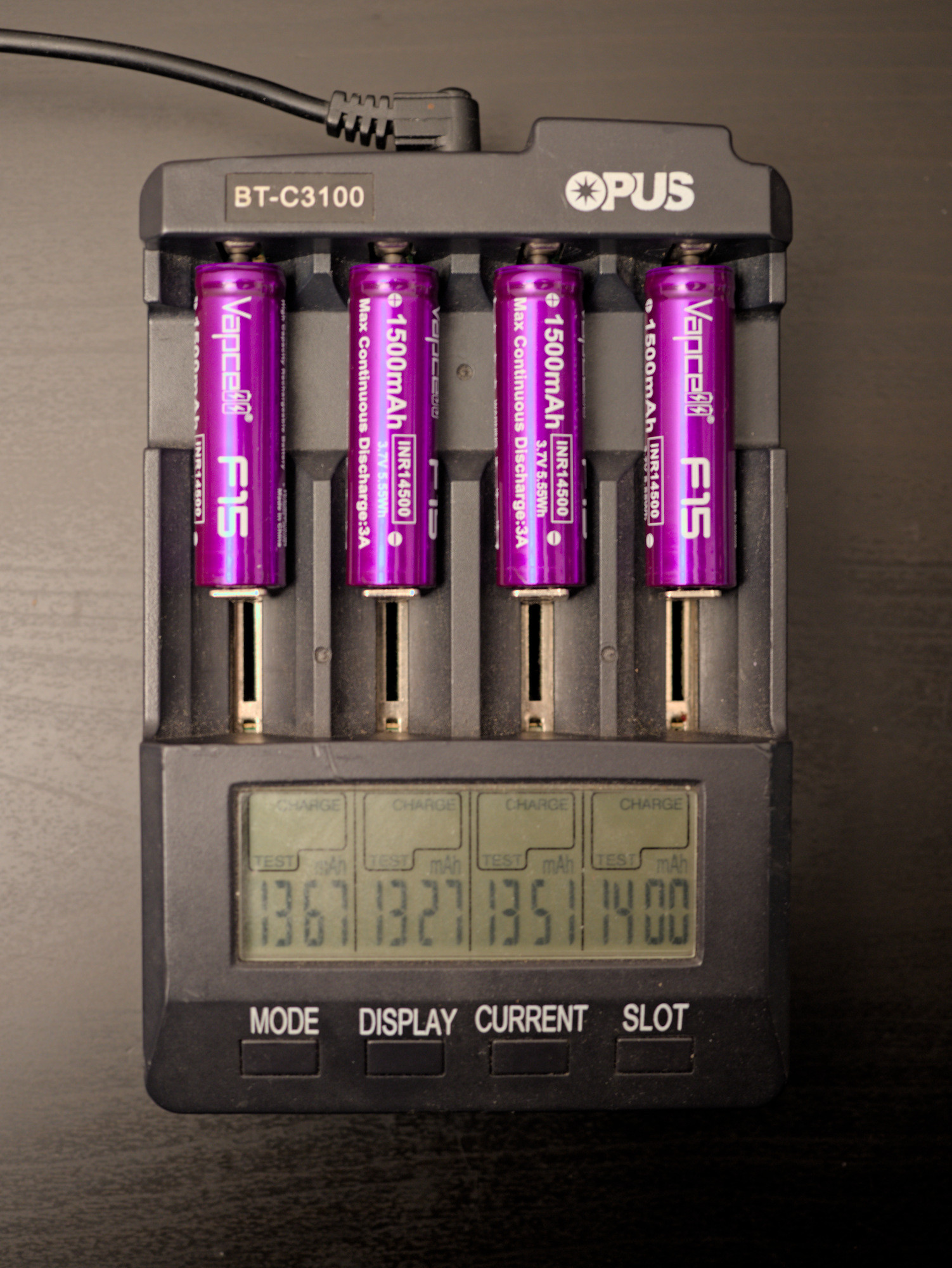 An Opus BT-C3100 battery charger with four Vapcell F15 14500 batteries. The display indicates charge test modes and tested capacity in mAh, which reads 1367, 1327, 1351, and 1400.