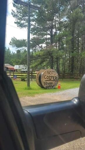 a huge roll of fibre optic cable going up a utility pole, the roll has a big text on it that says "NOT COPPER – FIBER OPTIC", probably to discourage thieves